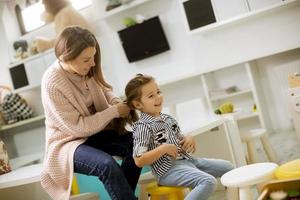 professeur de maternelle aidant une petite fille à réparer les cheveux dans la salle de jeux de la maternelle photo