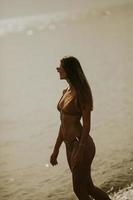 jeune femme en bikini marchant au bord de la mer sur un coucher de soleil de jour d'été photo