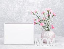 maquette cadre vide blanc, vase rond de fleurs d'oeillets et de gypsophile, lettres de maman en bois blanc. photo