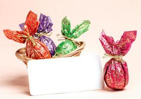 carte de voeux de pâques - oeufs enveloppés dans du papier de couleur et note blanche vide sur rose pastel. maquette. photo