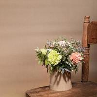 bouquet de fleurs dans un vase en carton bricolage écologique debout sur une vieille chaise en bois sur beige avec ombres et espace de copie. photo