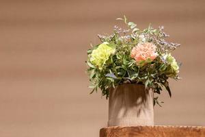composition écologique avec bouquet de fleurs dans un vase en carton bricolage debout sur une vieille table en bois sur beige avec des ombres.