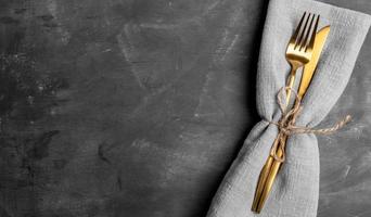 fourchette et couteau à couverts dorés dans une serviette grise sur fond gris foncé. maquette. bannière. vue de dessus. photo