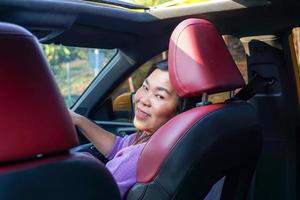 femme asiatique au volant d'une voiture jaune toit en boucle soleil ouvert sourire heureux elle a jeté un coup d'œil derrière elle, regardant à travers la porte arrière droite de la voiture. pendant la conduite d'un week-end. mise au point douce et sélective. photo
