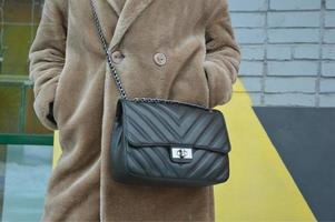 sac à main noir sur une chaîne sur le fond d'un manteau en fausse fourrure beige. accessoires féminins à la mode. éléments de vêtements pour femmes. photo