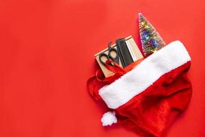 composition de noël à plat. outils de coiffure, cadeau et décor de noël dans un chapeau de père noël sur fond rouge. noël, bonne année photo