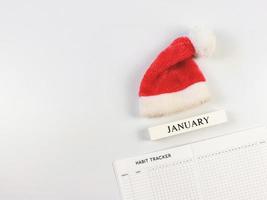 mise à plat du livre de suivi des habitudes, calendrier en bois janvier, bonnet de noel rouge sur fond blanc avec espace de copie. photo