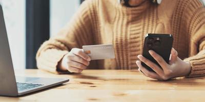 une jolie femme asiatique est assise à son bureau, tenant un smartphone et une carte de crédit. gros plan. paiement en ligne, paiement par carte de crédit, banque mobile, achats en ligne, société sans numéraire. photo