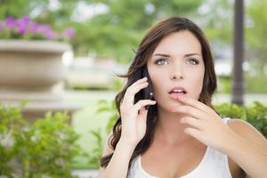 jeune femme adulte stupéfaite parlant sur un téléphone portable à l'extérieur photo