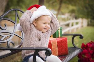 jeune enfant portant un bonnet de noel assis avec des cadeaux de noël à l'extérieur. photo