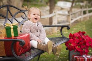 jeune enfant en bas âge assis sur un banc avec des cadeaux de noël à l'extérieur photo