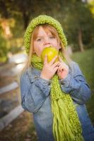 jeune fille portant un foulard vert et un chapeau mangeant une pomme à l'extérieur photo