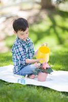 jeune garçon de race mixte arrosant ses fleurs en pot à l'extérieur sur l'herbe photo