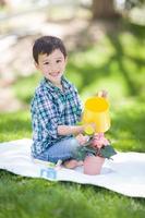 jeune garçon de race mixte arrosant ses fleurs en pot à l'extérieur sur l'herbe photo