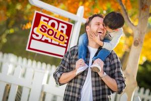 jeune métis chinois et caucasien père et fils devant le panneau immobilier vendu à vendre et la cour d'automne. photo