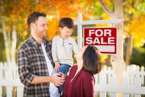 jeune famille mixte chinoise et caucasienne devant un panneau immobilier à vendre et une cour d'automne. photo