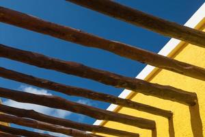 Poutres en bois abstraites et mur jaune vif contre le ciel bleu photo