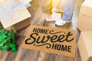 homme et femme debout près du tapis de bienvenue home sweet home, boîtes de déménagement et plante photo