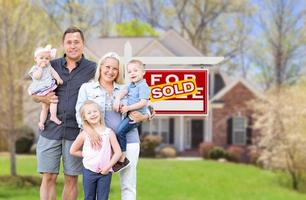 heureuse jeune famille caucasienne à l'extérieur devant leur nouvelle maison et enseigne immobilière vendue photo