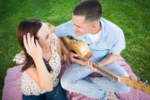 jeune homme adulte jouant de la guitare pour sa petite amie dans le parc. photo