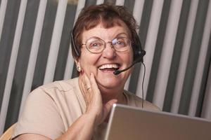 femme adulte senior souriante avec casque téléphonique et moniteur photo