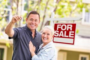 couple de race blanche devant l'enseigne immobilière à vendre et maison avec clés photo