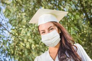 femme diplômée en bonnet et robe portant un masque médical photo