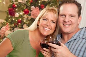 couple caucasien tenant des verres à vin devant l'arbre de noël décoré. photo