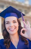 heureuse diplômée métisse femme en bonnet et robe célébrant sur le campus. photo