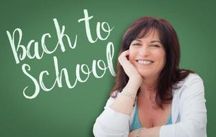 retour à l'école écrit sur un tableau vert derrière une femme d'âge moyen souriante photo