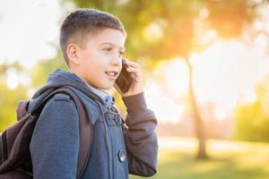 jeune garçon hispanique marchant à l'extérieur avec un sac à dos parlant sur un téléphone portable photo