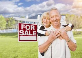 Heureux couple de personnes âgées devant le signe à vendre et la maison photo