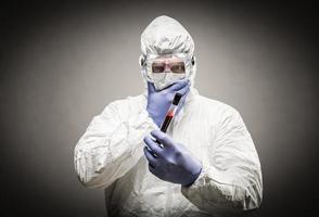 homme portant des vêtements de protection contre les matières dangereuses tenant un tube à essai rempli de sang sur fond gris. photo