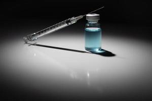 aiguille de seringue et flacon de médicament avec tache chimique bleu clair éclairée sur fond réfléchissant photo
