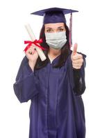 femme diplômée portant un masque médical et une casquette et une robe donne un coup de pouce isolé sur fond blanc photo