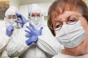 femme adulte âgée portant un masque médical dans le bureau du médecin avec des infirmières en combinaisons de matières dangereuses derrière photo