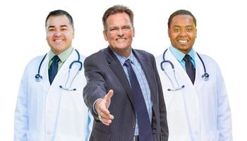 médecins de race mixte derrière l'homme d'affaires atteignant pour serrer la main sur blanc photo