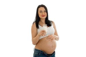 Jeune fille brune enceinte avec un verre de lait en regardant la caméra isolée sur fond blanc photo