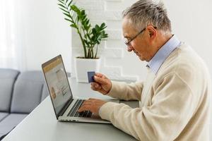 homme senior à l'ordinateur portable payant par carte de crédit pour les achats en ligne photo