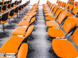 intérieur de la salle de réunion. vue de face de rangées de chaises orange debout dans un auditorium. sièges dans une salle de conférence vide. immense hall intérieur avec tapis et lumières comme salle de conférence dans un hôtel de luxe. photo