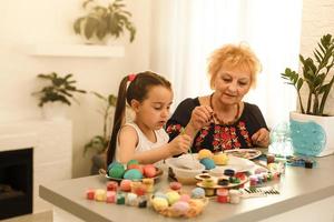 jeune femme joyeuse et sa petite fille regardant à travers des oeufs de pâques peints et en choisissant un pour grand-mère photo