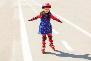 Petite jolie fille sur patins à roulettes en casque dans un parc photo