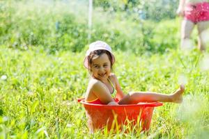 développement de l'enfant en harmonie avec la nature. petite belle fille s'amusant avec de l'eau et prenant un bain à l'extérieur sur l'herbe dans un bol à vaisselle vintage hygiène, enfance heureuse, concept nature photo