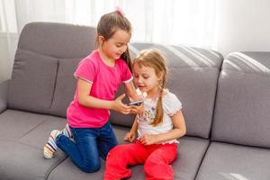 concept de personnes, d'enfants, de technologie, d'amis et d'amitié - petites filles heureuses assises sur un canapé et prenant un selfie avec un smartphone à la maison. photo