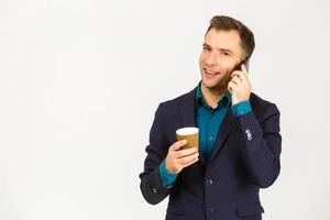 portrait d'un jeune homme d'affaires souriant utilisant un smartphone et tenant une tasse de café isolé sur fond blanc photo