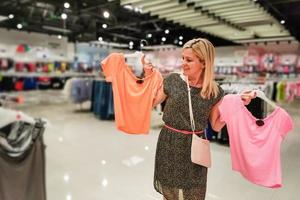 concept de vente, de mode, de consommation et de personnes - jeune femme heureuse choisissant des vêtements dans un centre commercial ou un magasin de vêtements photo