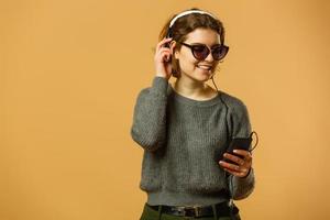 femme souriante écoutant de la musique dans des écouteurs et utilisant un smartphone sur fond jaune photo