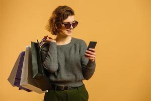 mode jolie jeune fille cool avec des sacs à provisions portant un chapeau noir pantalon blanc sur fond orange coloré photo