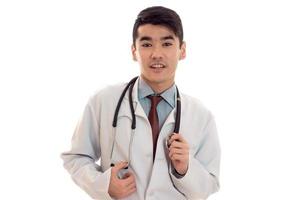 jeune médecin brune élégante en uniforme avec stéthoscope regardant la caméra et souriant isolé sur fond blanc photo