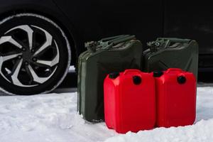 quatre bidons d'essence se tiennent dans la neige contre la voiture. photo